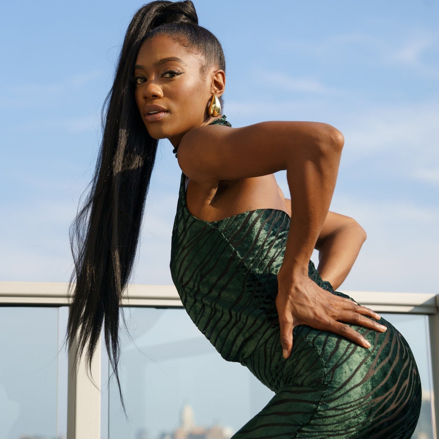 Woman in a green dress standing on a balcony with a cityscape in the background